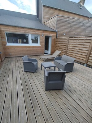 Eine Holzterrasse mit Gartenmöbeln, einem Fenster und einer Tür.