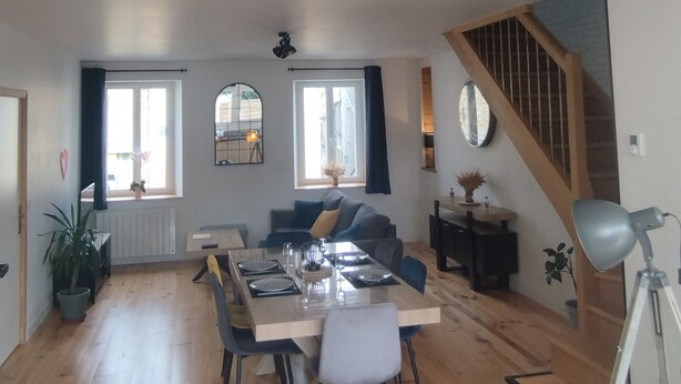 Amplia sala de estar con una mesa de comedor, vigas de madera, una escalera y ventanas grandes.