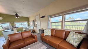 A living room with a brown leather sofa, a wooden coffee table, and a view of the outside. - Sargent Sunset & Fishing Retreat (Bay City)