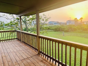 Una terraza de madera con barandilla, un césped y casas al fondo.