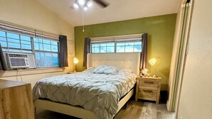 A bedroom with a bed, bedside lamps, a ceiling fan, a window with curtains, and an air conditioning unit. - Sargent Sunset & Fishing Retreat (Bay City)