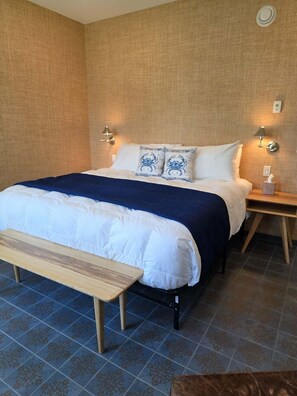 Hotellihuone, jossa on sänky, yöpöydät, penkki ja kuviollinen lattialaatoitus.