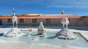 A salt flat with three white statues, a building with a red roof, and a sign reading 'Dakini Potos.' - Hostal Terra Sal (Uyuni)