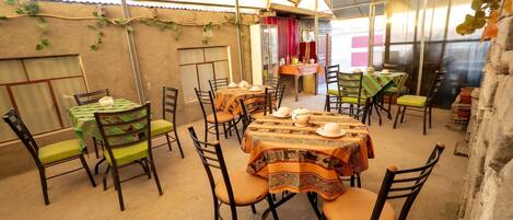 An indoor dining area with tables and chairs, covered by a translucent roof, and walls adorned with plants.