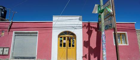 A building with a red facade, a yellow door, and a closed metal shutter.
