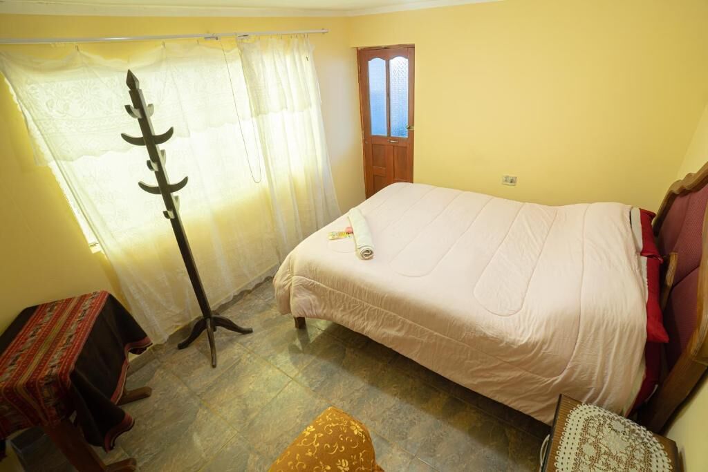 A bedroom with a bed, a window with curtains, a door, and a small table.