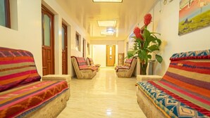 A hotel corridor with patterned sofas, a potted plant, and a door at the end. - Hostal Terra Sal (Uyuni)