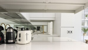 Une cuisine moderne avec des meubles blancs, une bouilloire en acier inoxydable, un grille-pain et une machine à café.