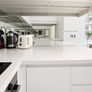 Eine moderne Küche mit weißen Schränken, einem Edelstahl-Wasserkocher, einem Toaster und einer Kaffeemaschine.