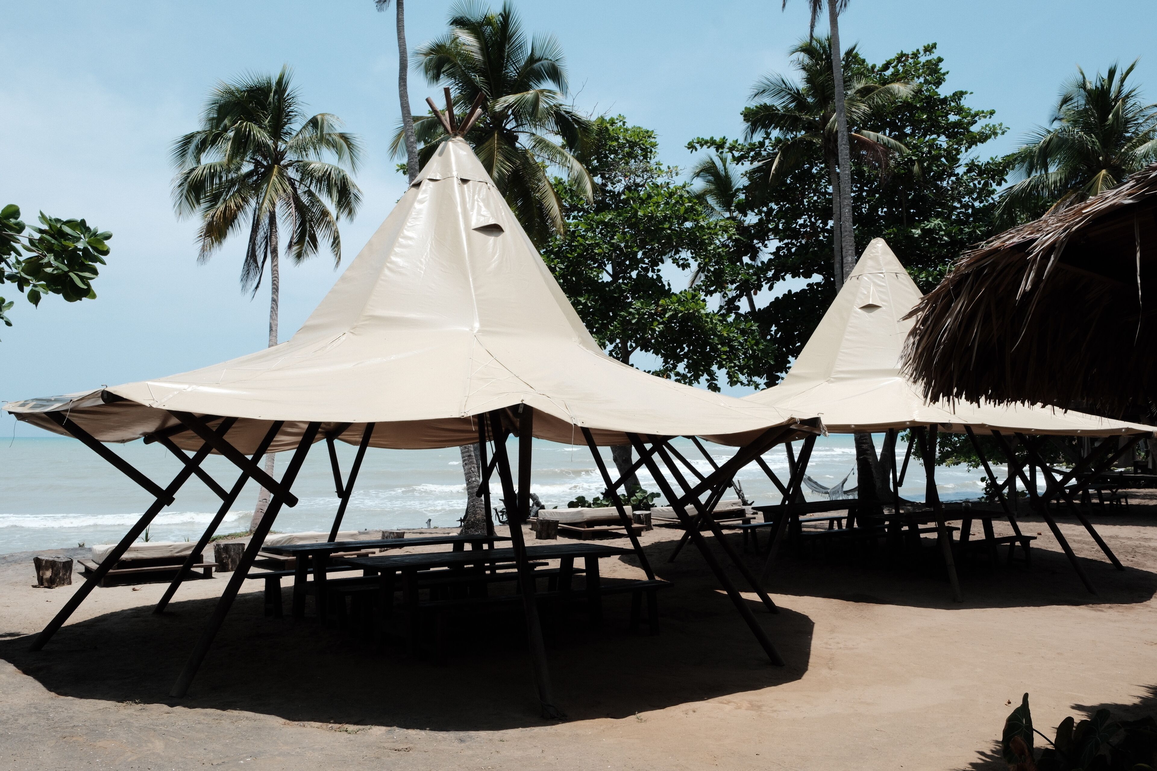 Une plage avec une structure à toit de chaume et un auvent en forme de tente.