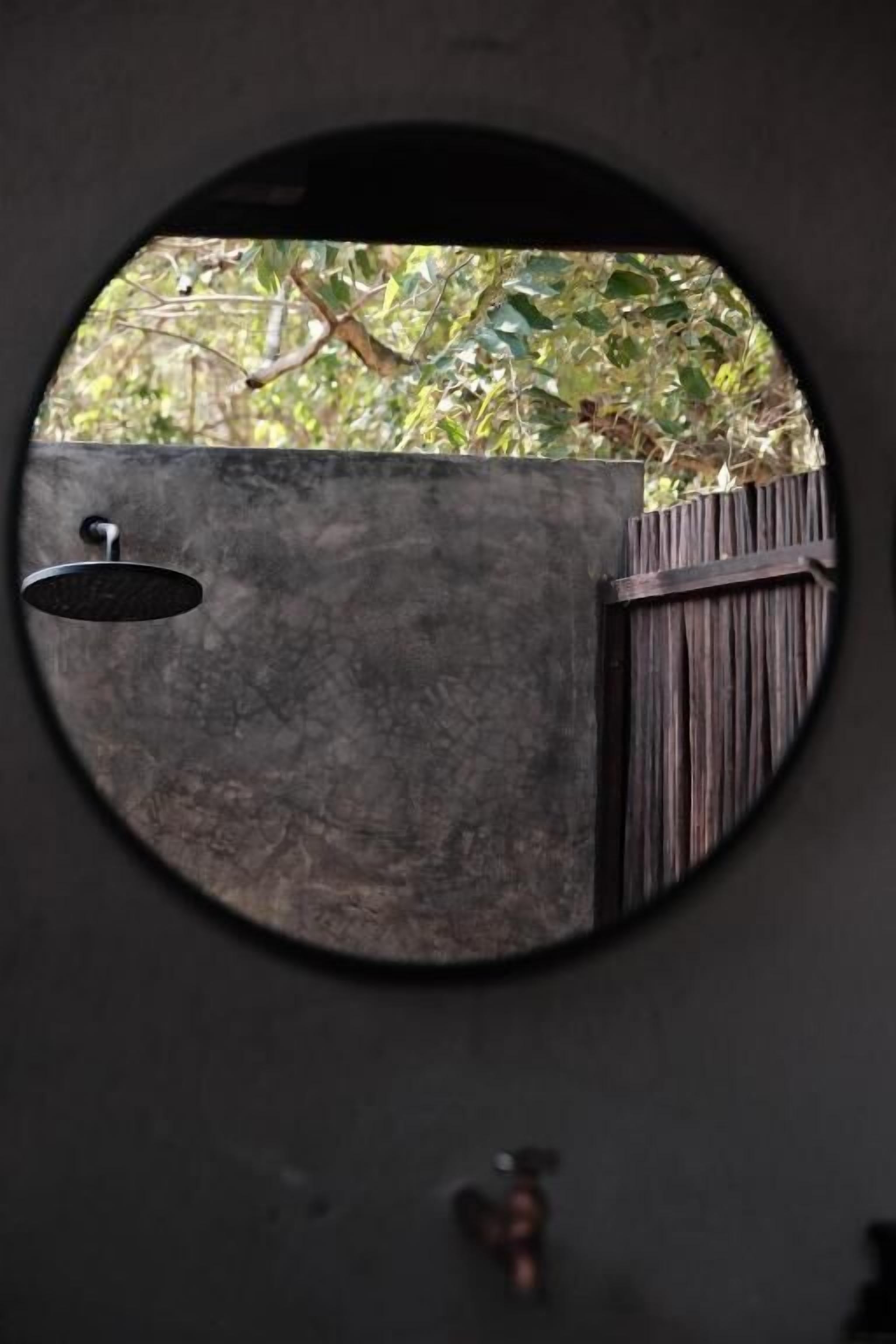 Una finestra circolare con vista su una recinzione in legno e vegetazione.