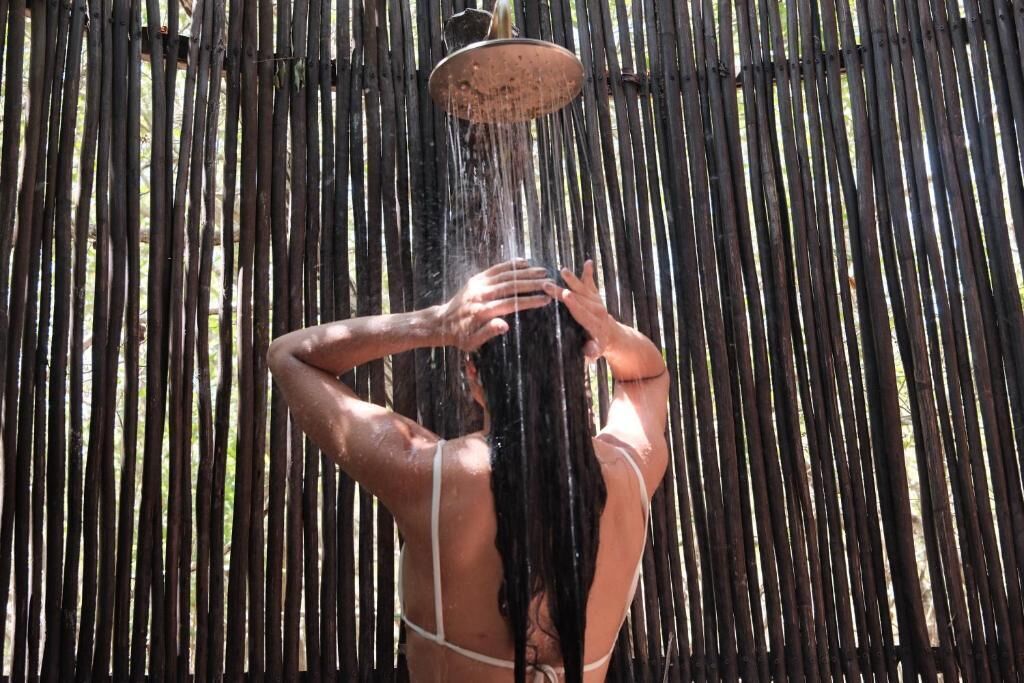 A person taking a shower under a bamboo showerhead.