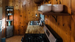 A wooden interior with a kitchen area featuring a stove, sink, and shelves with dishes. - 2 BR 2 BA San Juan Mountain Cabin (Archuleta County)