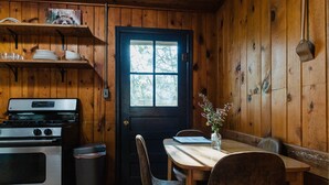 A wooden cabin interior with a kitchen, dining table, chairs, and a window. - 2 BR 2 BA San Juan Mountain Cabin (Archuleta County)