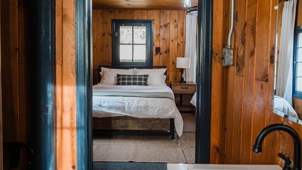 Quarto de cabana de madeira com cama, mesa de cabeceira e janela.