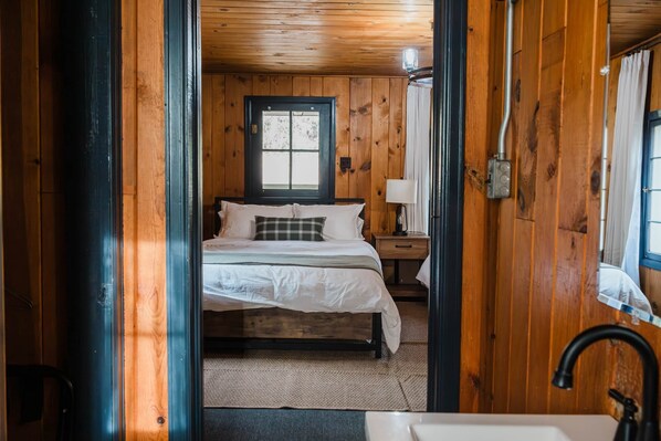 A wooden cabin bedroom with a bed, nightstand, and window.