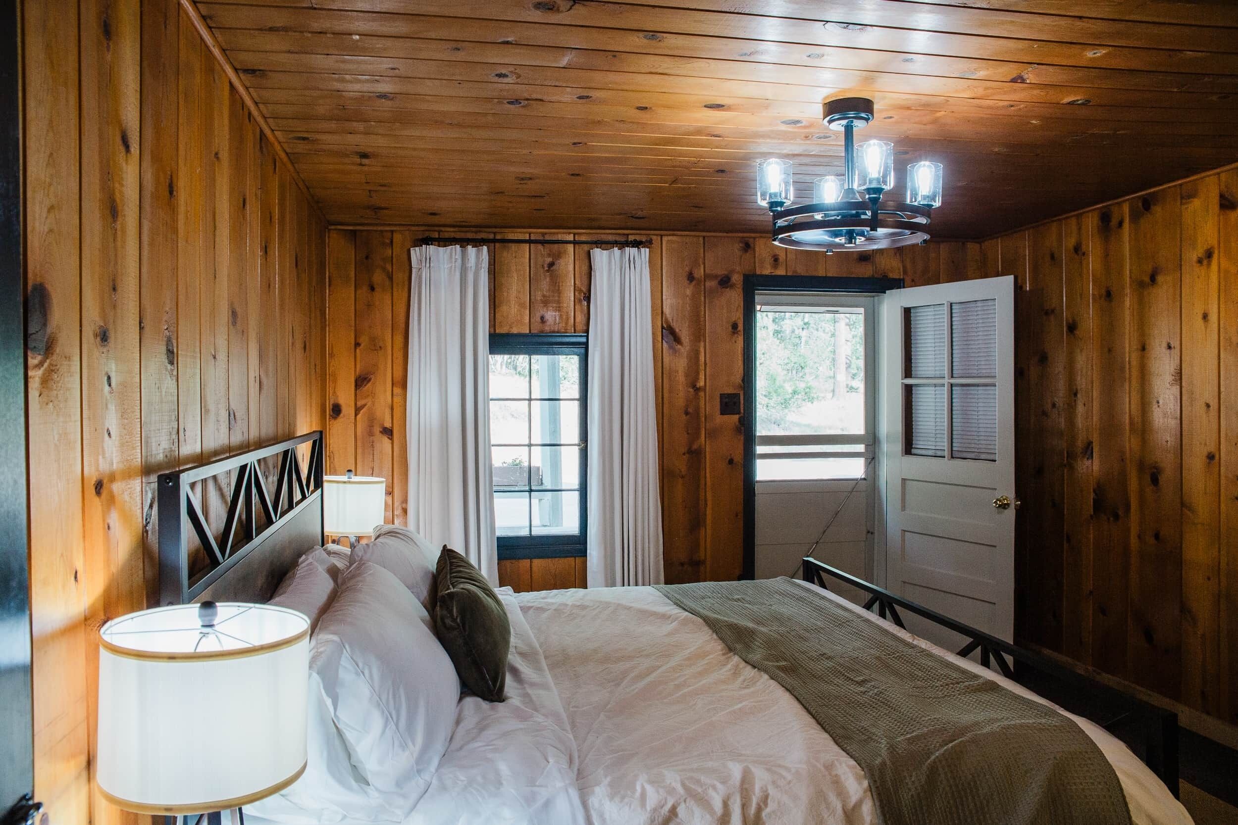 A wooden-paneled bedroom with a bed, curtains, a chandelier, and a door.