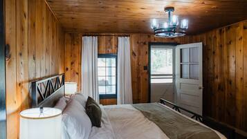 A wooden-paneled bedroom with a bed, curtains, a chandelier, and a door.