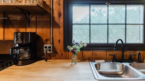 Uma cozinha com cafeteira, um vaso de flores e uma janela com vista para árvores.