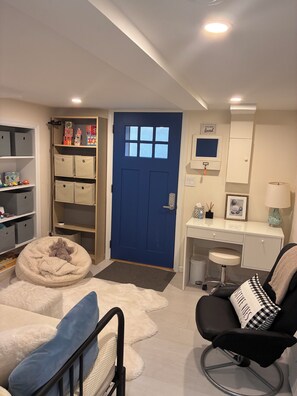 Ein Zimmer mit blauer Tür, weißem Schreibtisch, schwarzem Stuhl, einem flauschigen weißen Teppich und Stauraumeinheiten.