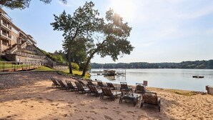 A beach with sun loungers, a lake, and a building with balconies.