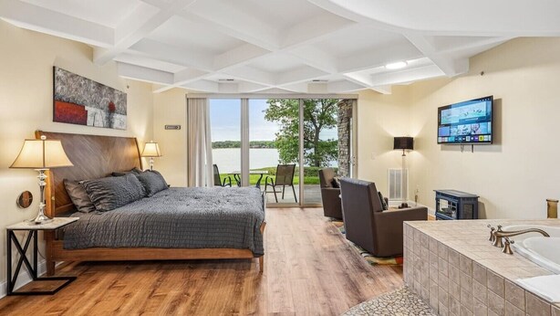 A bedroom with a bed, a TV, a bathroom with a bathtub, and a view of the outdoors.
