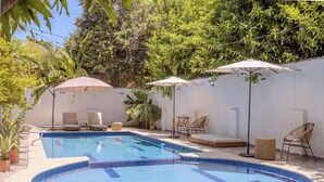 A swimming pool with lounge chairs and umbrellas, surrounded by greenery and a white wall.