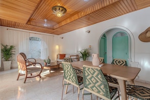 A dining area with a wooden ceiling, a table, chairs, and a green door.