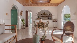 A spacious room with a wooden ceiling, a dining area with a table and chairs, and a kitchen visible through an archway.