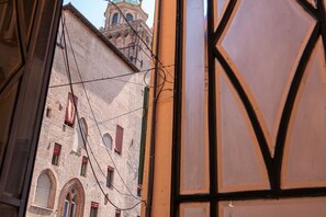 A view through a window with a building facade, including a tower with a dome and arched windows. - Enjoy a stylish holiday in this space in the heart of Bologna. A modern apartment welcomes you in the heart of Bologna's historic center, overlooking Piazza Maggiore. Located on the first floor of a typical Bolognese building, the apartment features a sp (Bologna)