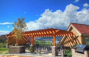 A covered outdoor seating area with stone planters, a grill, and a view of the landscape. - Spacious Waterfront Condo! Walk to Downtown (Kelowna)