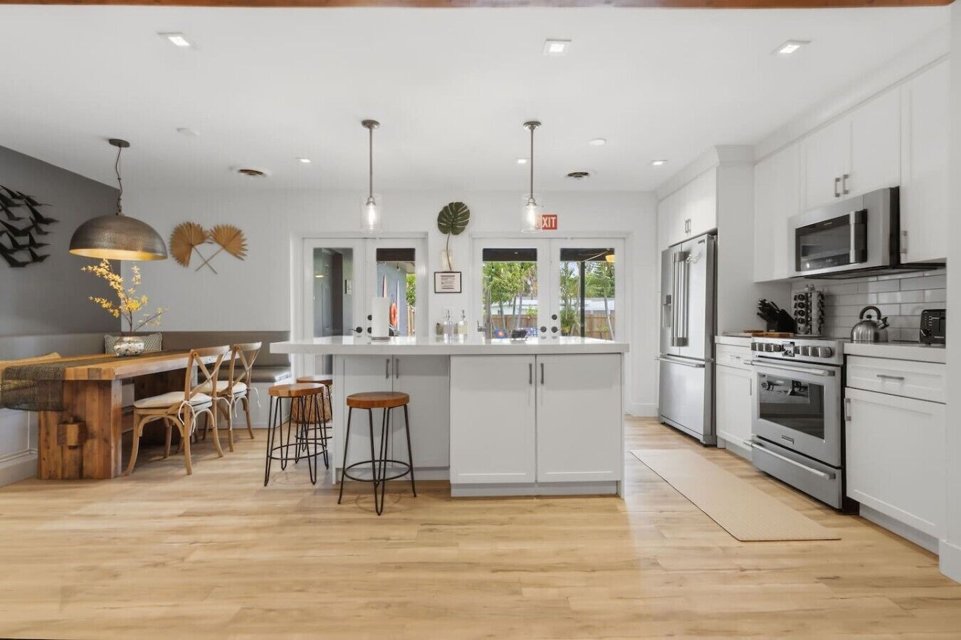 A modern kitchen with white cabinets, stainless steel appliances, a wooden dining area, and pendant lighting.