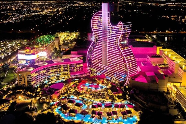 Ein großes Hotel mit einem auffälligen, gitarrenförmigen Gebäude, mehreren Schwimmbecken und einem gut beleuchteten Außenbereich.