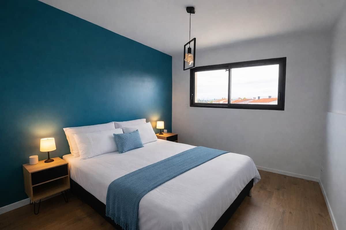 A bedroom with a bed, bedside lamps, a window, and a view.