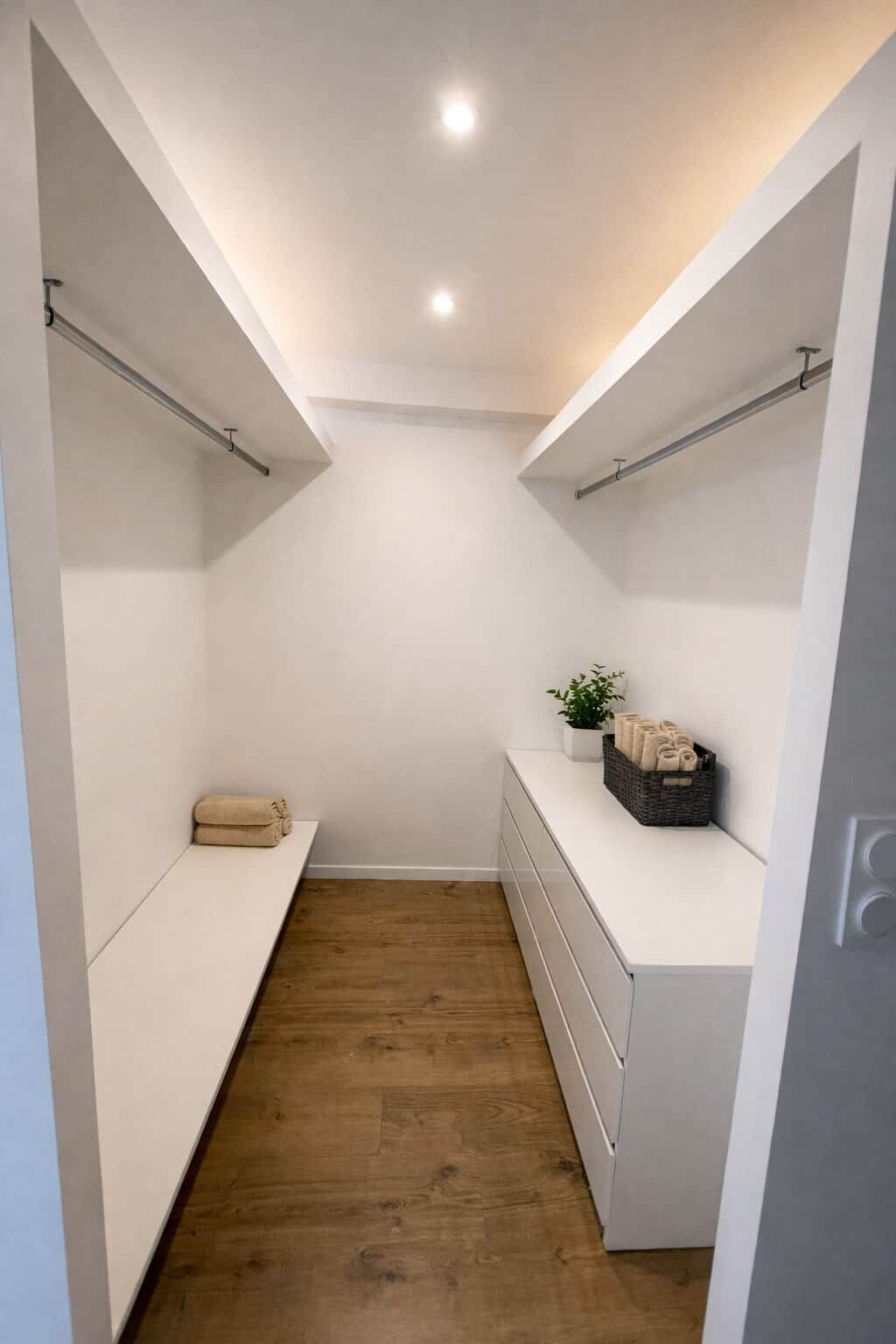 A narrow walk-in closet with wooden flooring, white walls, and built-in shelving.