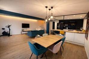 A modern kitchen with a dining area, a TV, and an exercise bike.