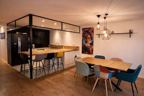A modern kitchen with a wooden island, bar stools, and a dining table with colorful chairs. - Villa Baléares: Private Pool, Air Conditioning, WiFi, Parking, Golf Course & Lake (Villeneuve-de-la-Raho)