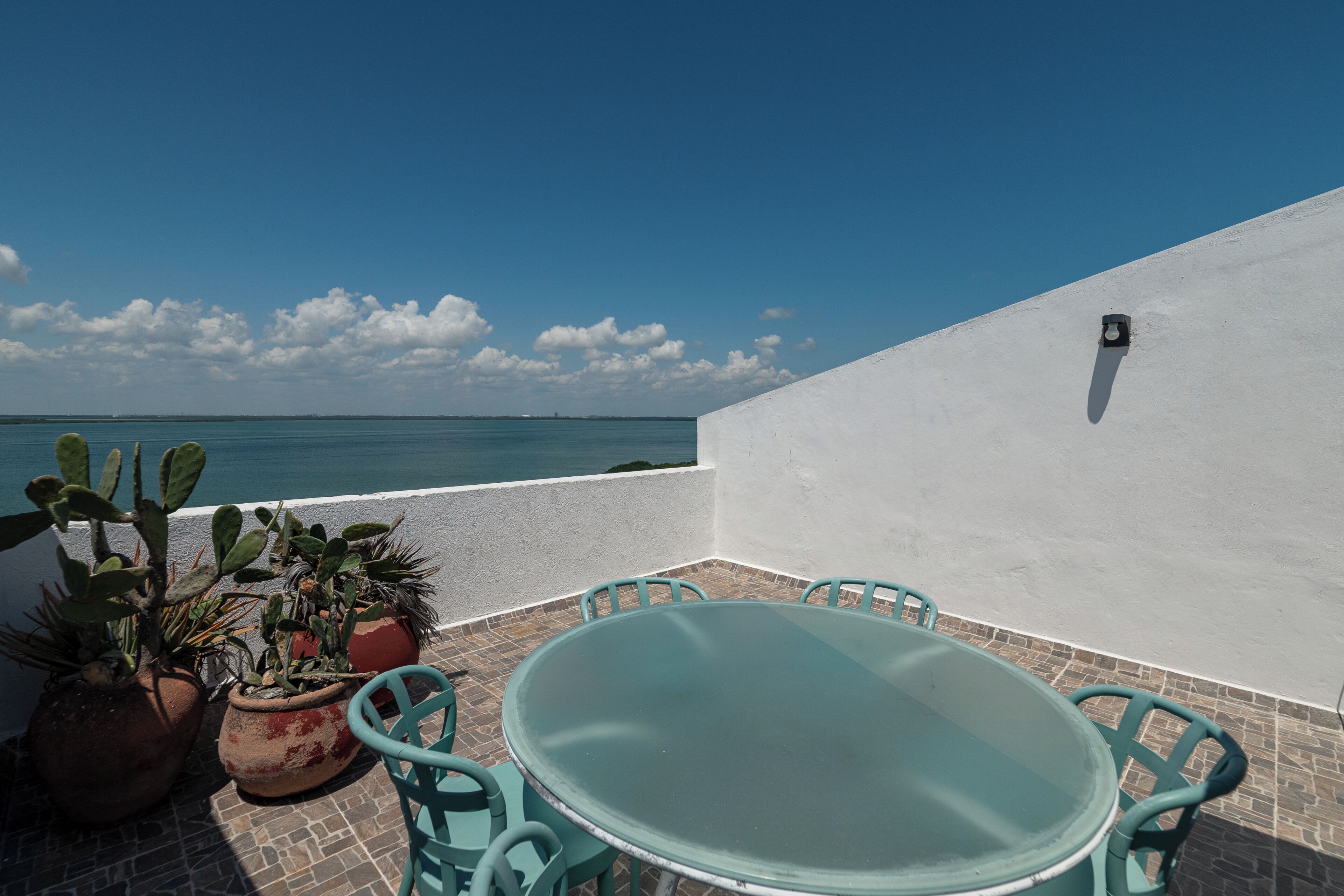A terrace with a table and chairs, potted plants, and a view of the sea.