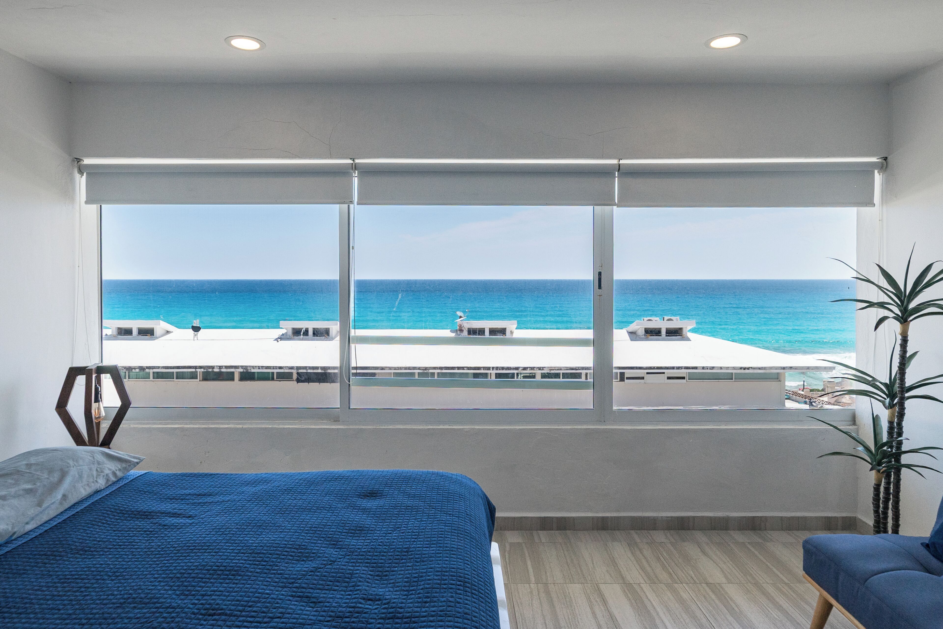 A hotel room with a large window offering a view of the sea and a rooftop bar.