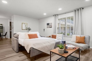 A modern hotel room with a bed, a sofa, a dining area, and a window with a view. - Modern Apartment near The Domain (Austin)
