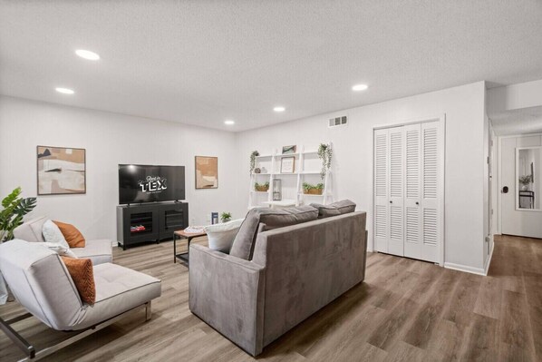 A modern living room with a grey sofa, a white armchair, a flat-screen TV, and a bookshelf. - Modern Apartment near The Domain (Austin)