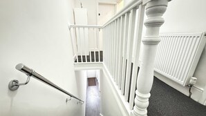 A staircase with white railings and a handrail, leading to a landing with a door.