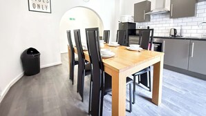 A modern kitchen with a wooden dining table, black chairs, and a sign that reads 'GOOD VIBES ONLY'.
