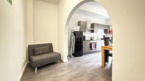A modern living room with a sofa, an archway leading to a kitchen with appliances and cabinets.