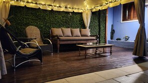 A cozy outdoor seating area with a sofa, chairs, and a table, surrounded by greenery and string lights. - Recanto da Dona Luiza - Pousada (Florianópolis)