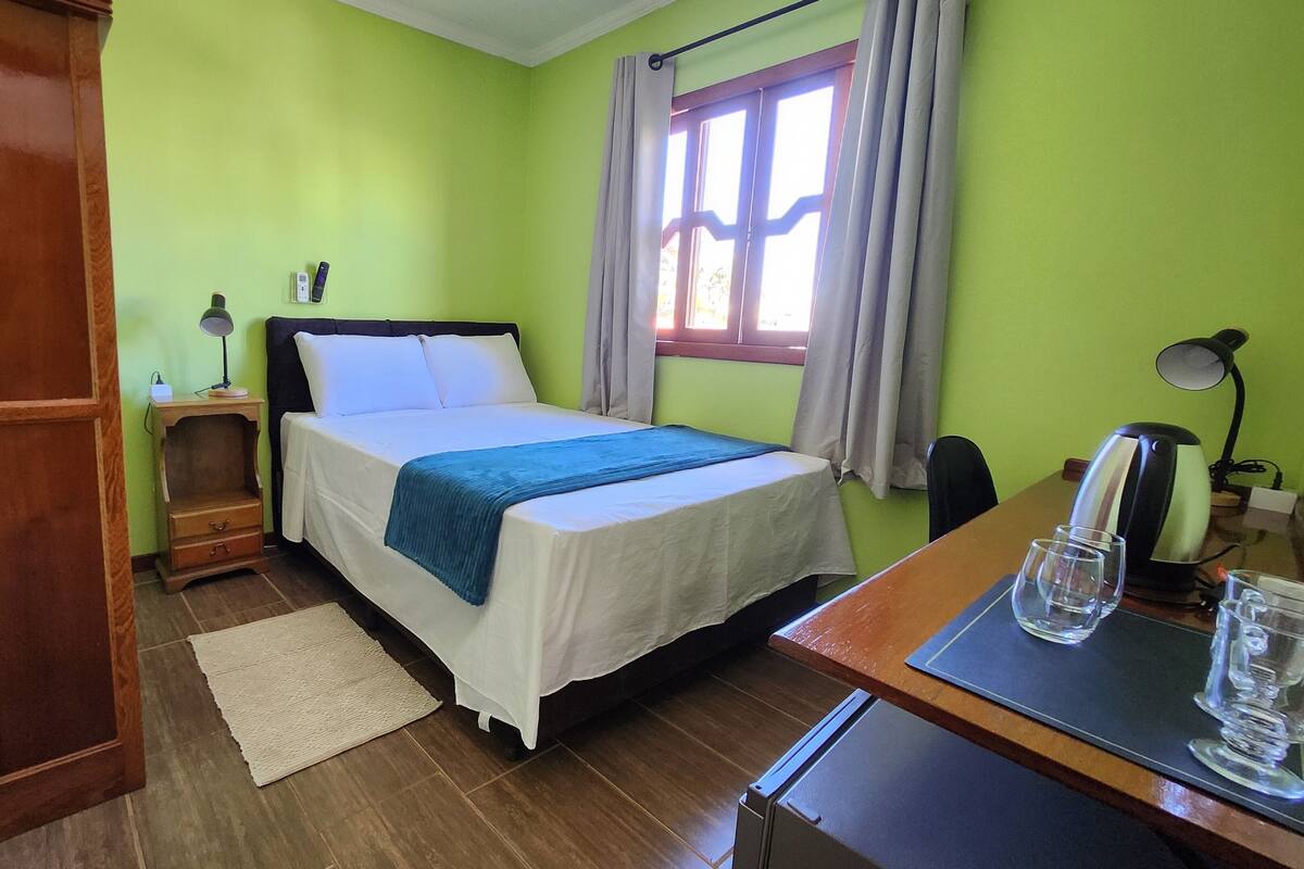 Una habitación con cama, mesita de noche, lámpara y ventana con cortinas.