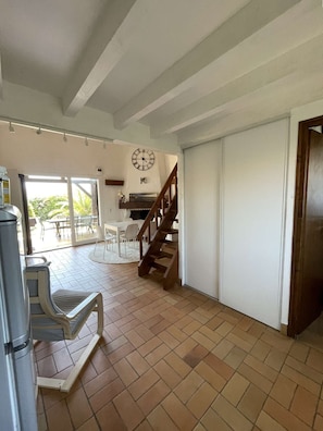 A spacious living area with a wooden staircase, a dining table, and a large clock on the wall. - Hossegor – Villa between the lake and the ocean, within walking distance of the beach – Sleeps 6 – Wi-Fi and air conditioning (SOORTS HOSSEGOR)
