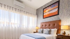 A bedroom with a large bed, a ceiling fan, an air conditioning unit, a nightstand with a lamp, and a painting on the wall. - Hidden Gem 1BR Near Romantic Zone (Puerto Vallarta)