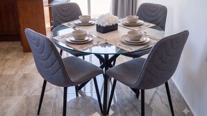 A round glass table with four grey upholstered chairs, each with a bowl and spoon on a placemat. - Hidden Gem 1BR Near Romantic Zone (Puerto Vallarta)