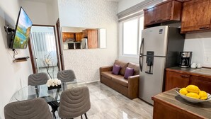 A modern kitchen with a refrigerator, coffee maker, and a dining area with a glass table and chairs. - Hidden Gem 1BR Near Romantic Zone (Puerto Vallarta)